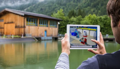 Tablet mit 3D-Modell der Turbinenanlage vor dem Gebäude des Wasserkraftwerks Warmatsgund in Oberstdorf
